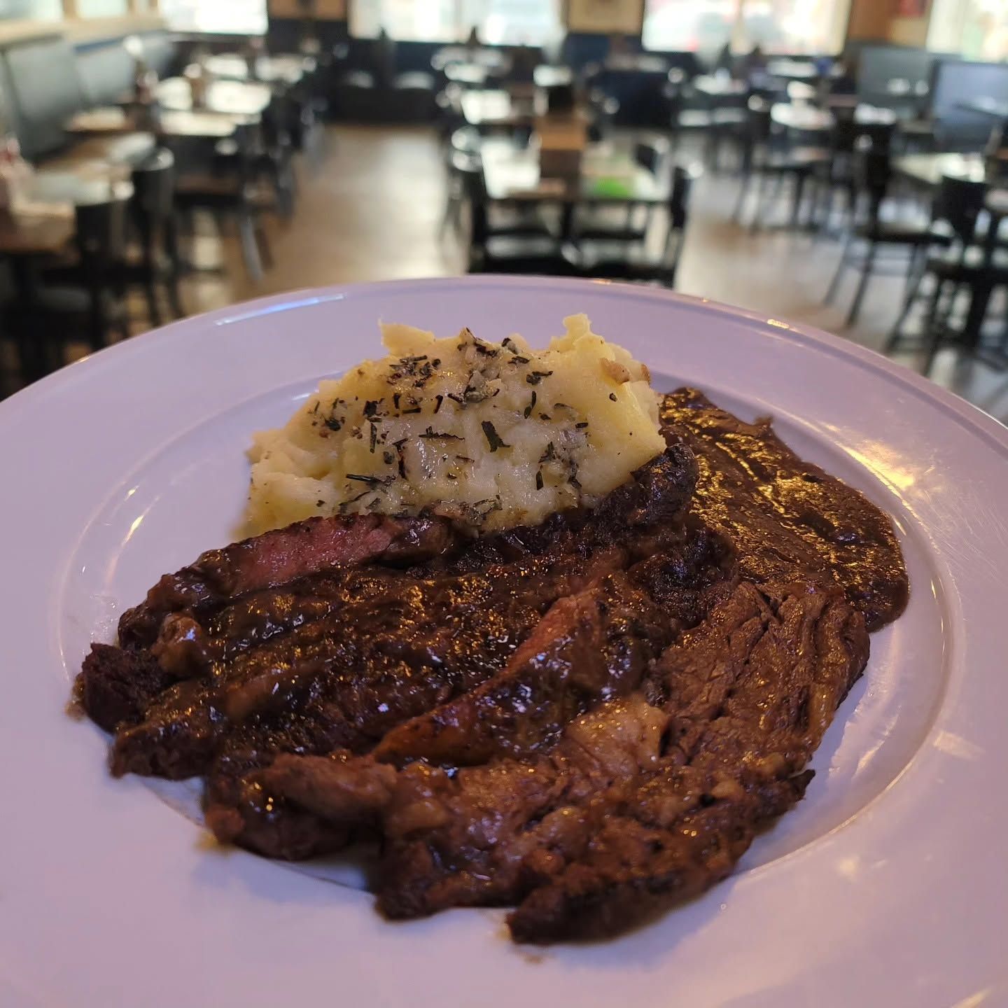 Grilled steak topped with mashed potatoes on a white plate in a restaurant dining room