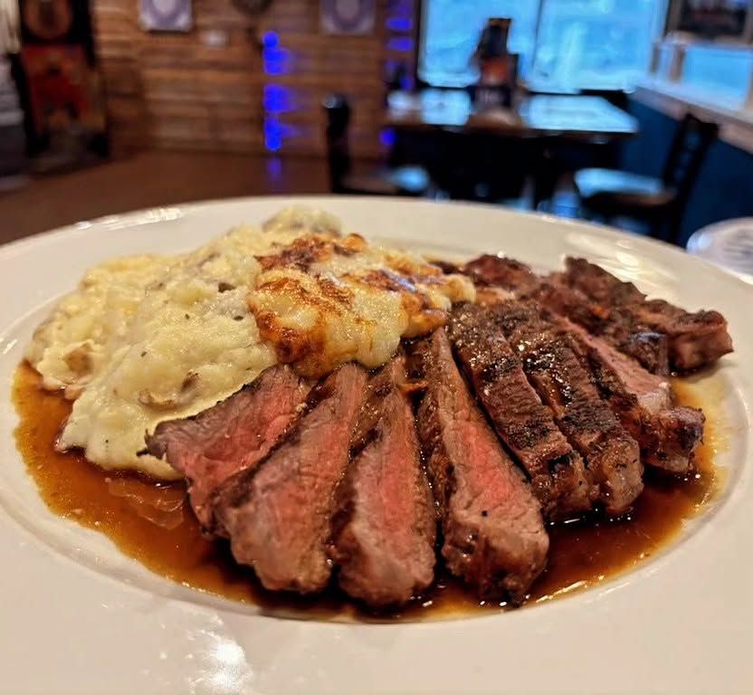 Sliced steak with mashed potatoes and gravy on a white plate in a restaurant setting
