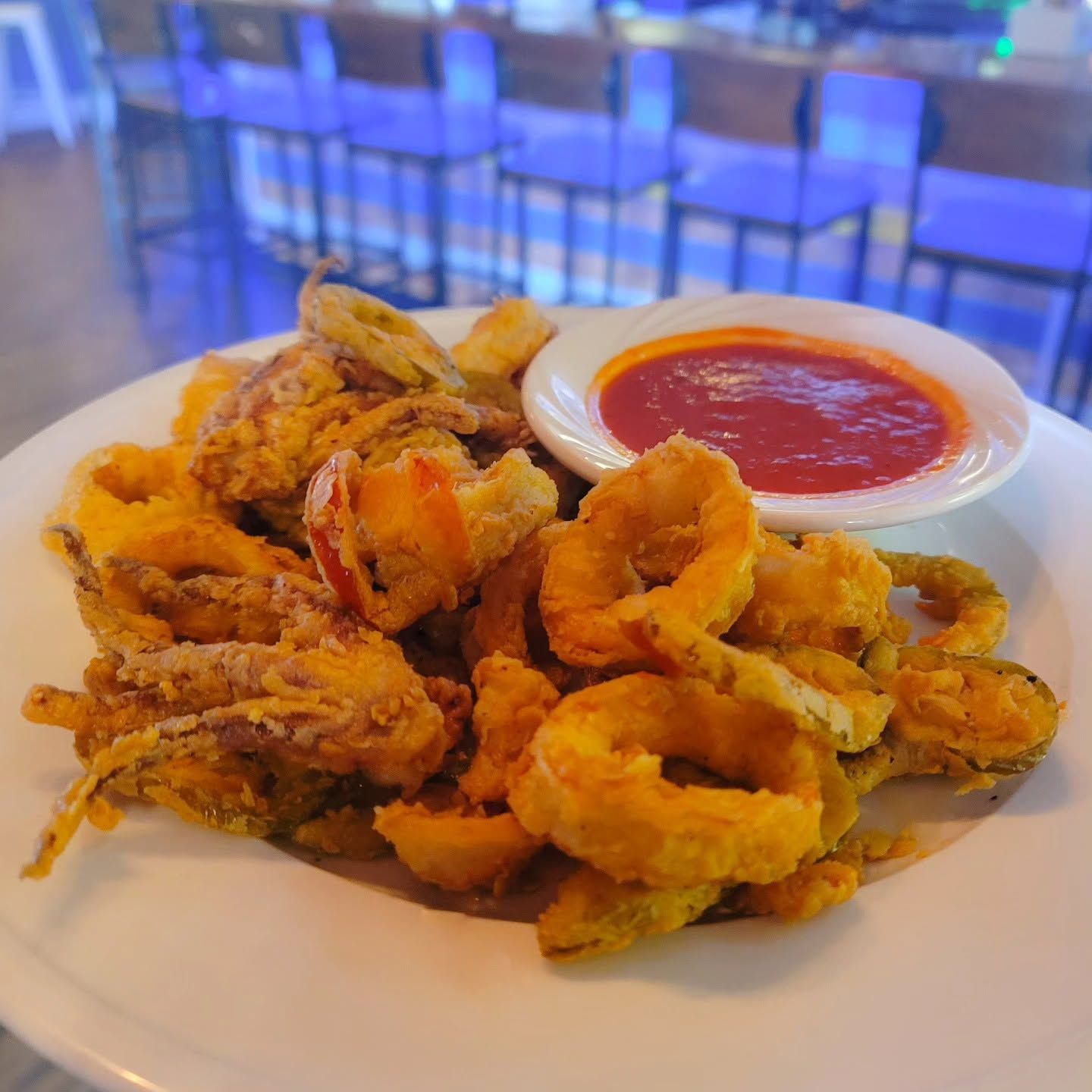 Plate of fried calamari with red dipping sauce on a table in a blurred restaurant setting