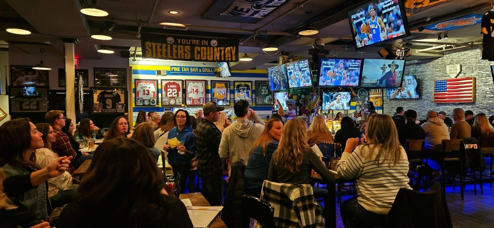 Crowded sports bar with patrons seated at tables, watching multiple TVs on the wall