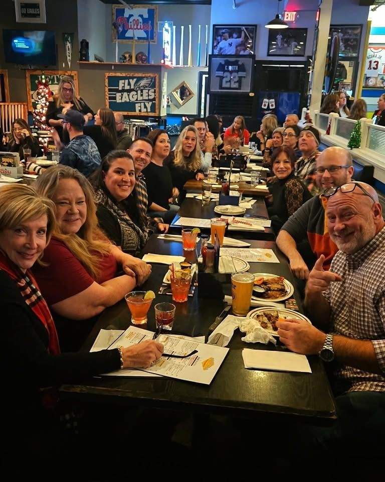 Group of people seated at a long table in a lively sports bar, smiling and eating together.