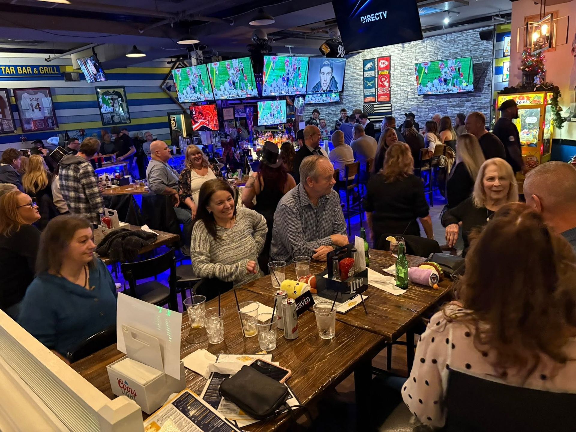 Crowded sports bar with diners at tables and multiple TVs showing games under colorful lights