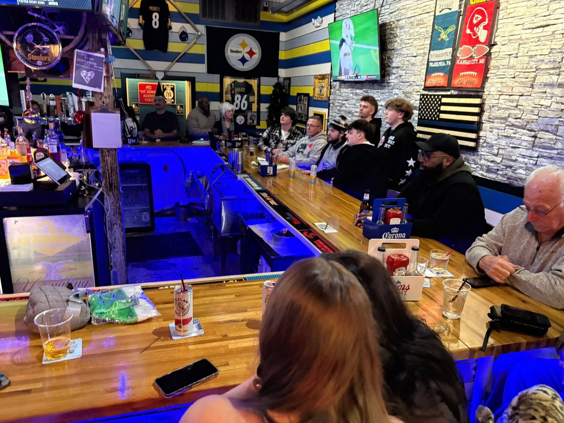 People seated at a blue-lit bar in a lively pub with wall decor and sports banners