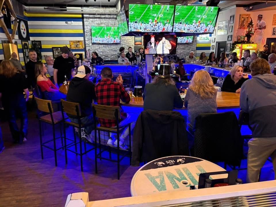 Sports bar with patrons seated at high tables watching multiple TV screens under blue lighting.