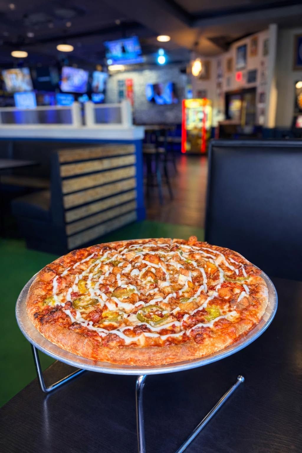Pizza on a stand in a dimly lit restaurant with blue chairs and bar seating in the background