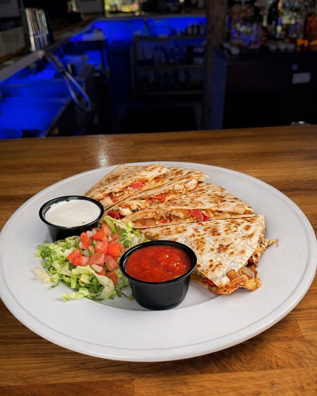 Grilled quesadilla with salsa, sour cream, and side salad on a white plate at a restaurant table
