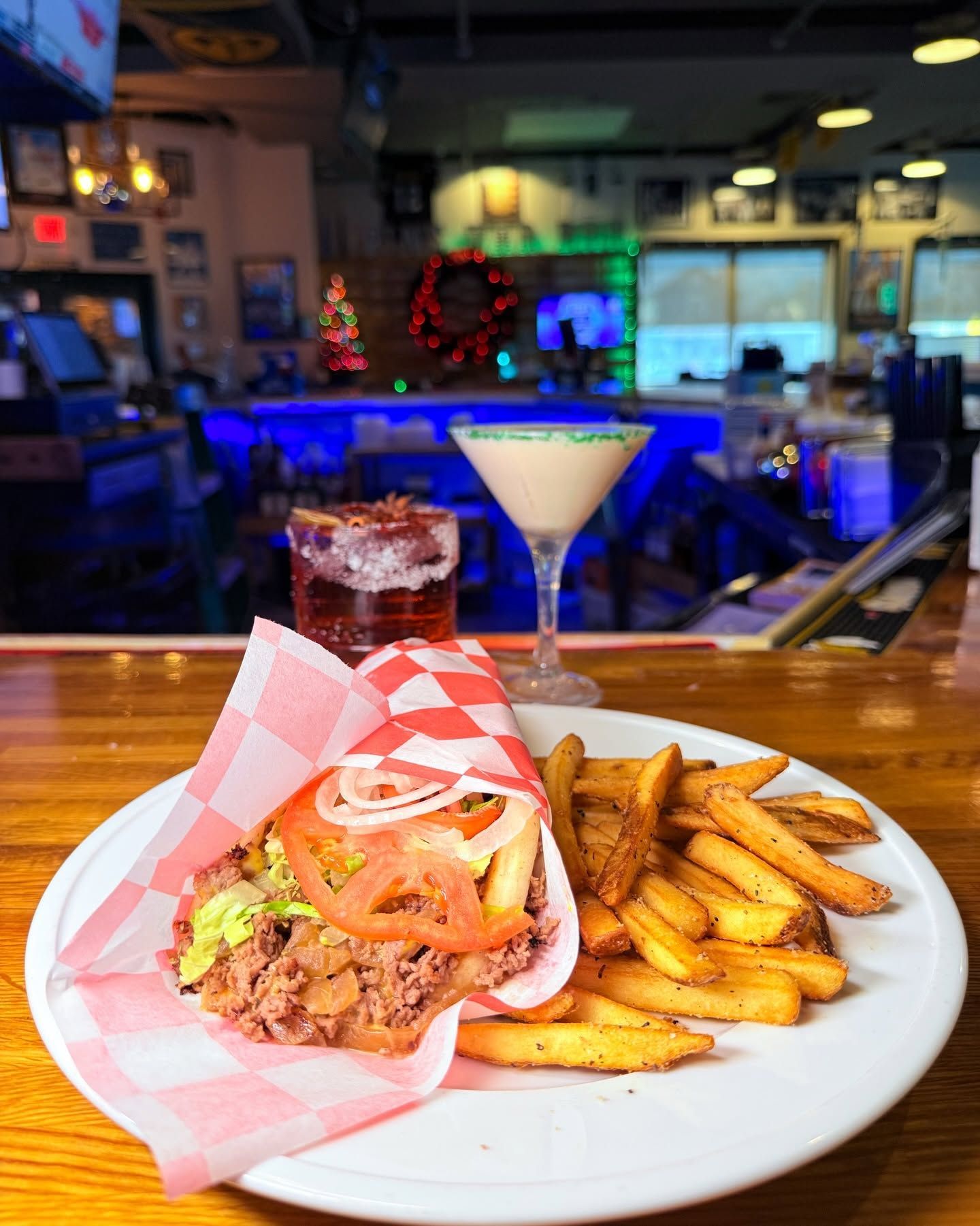 Taco and fries on a plate with a cocktail on a bar table in a dimly lit restaurant