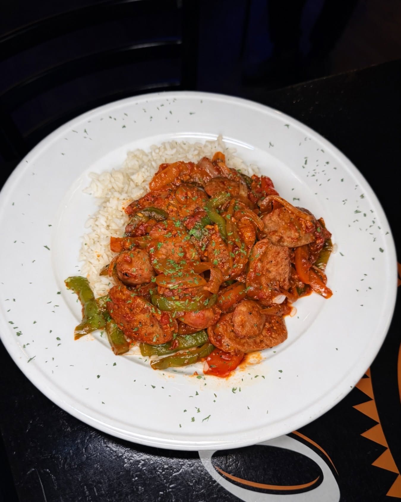 White plate of rice topped with red saucy stir-fry and green peppers on a dark table