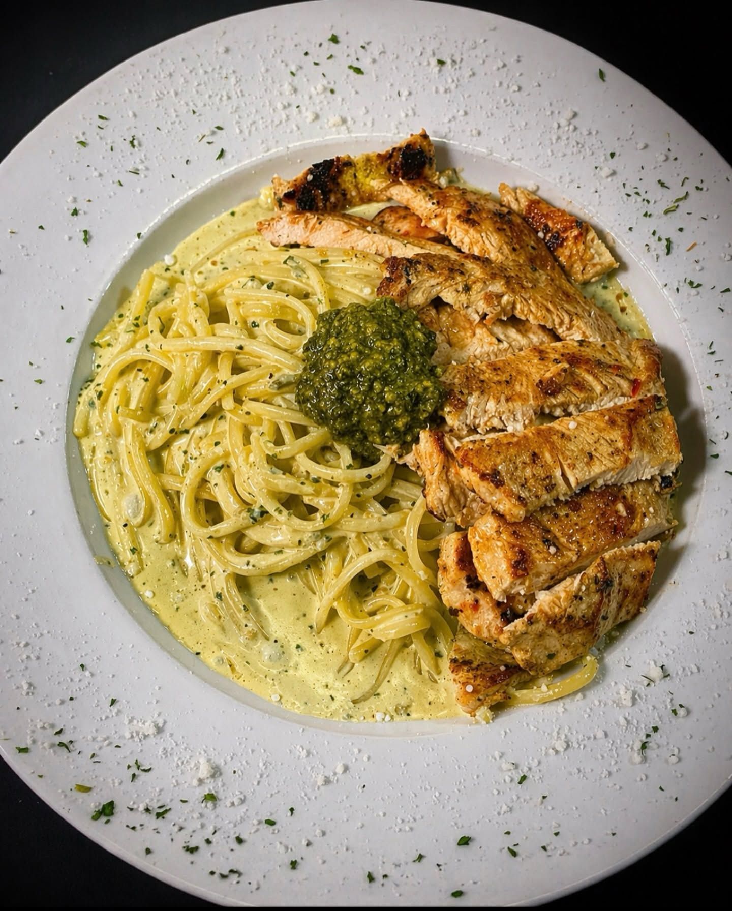 Creamy pasta with grilled chicken, topped with pesto on a white plate