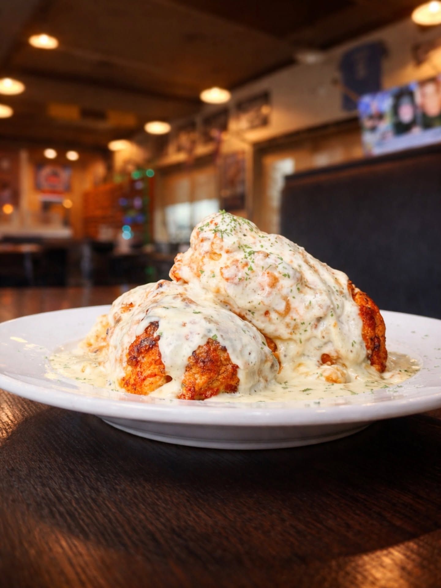 Plated fried chicken topped with creamy white sauce and herbs on a wooden table in a cozy restaurant