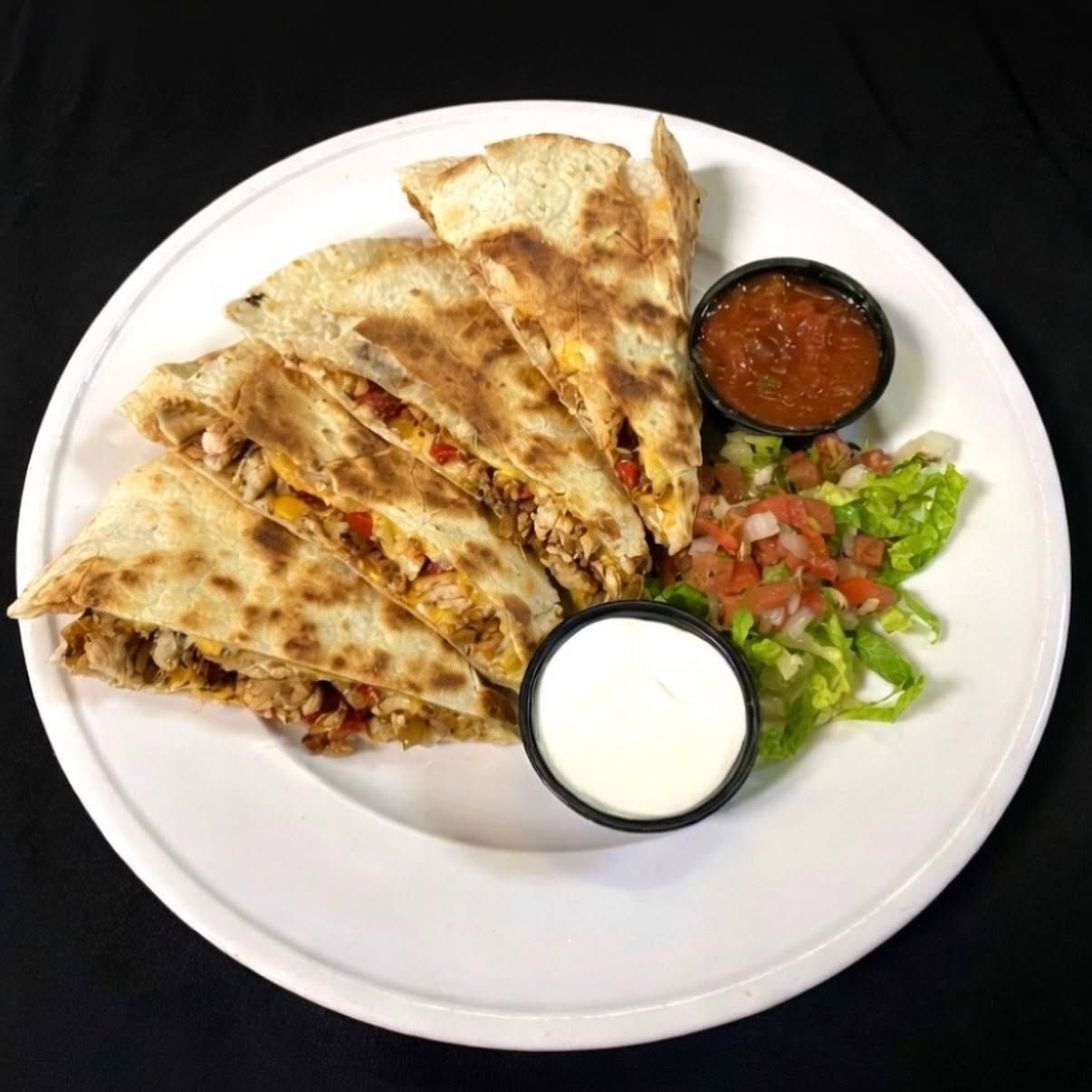 Quesadilla wedges on a white plate with salsa, sour cream, and lettuce-tomato garnish