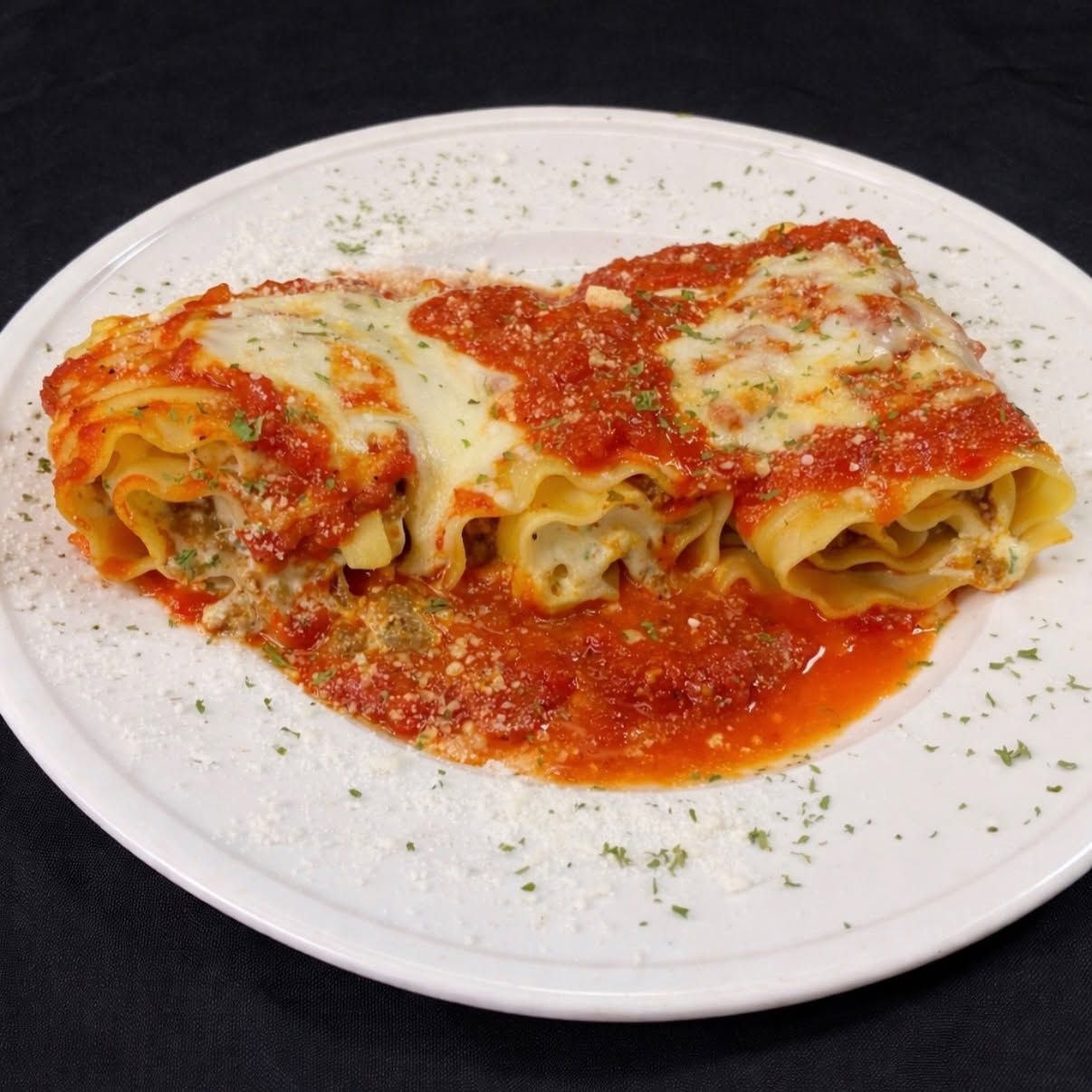 Two cheese-topped pasta rolls on a white plate with tomato sauce and grated herbs