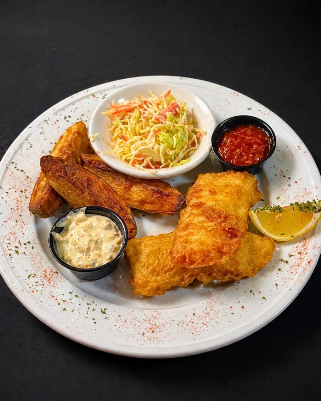 Fried chicken and sides on a white plate with coleslaw, sauces, and lemon wedge