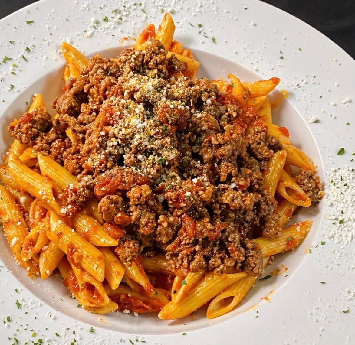 Plate of penne pasta topped with meat sauce and grated cheese on a white plate