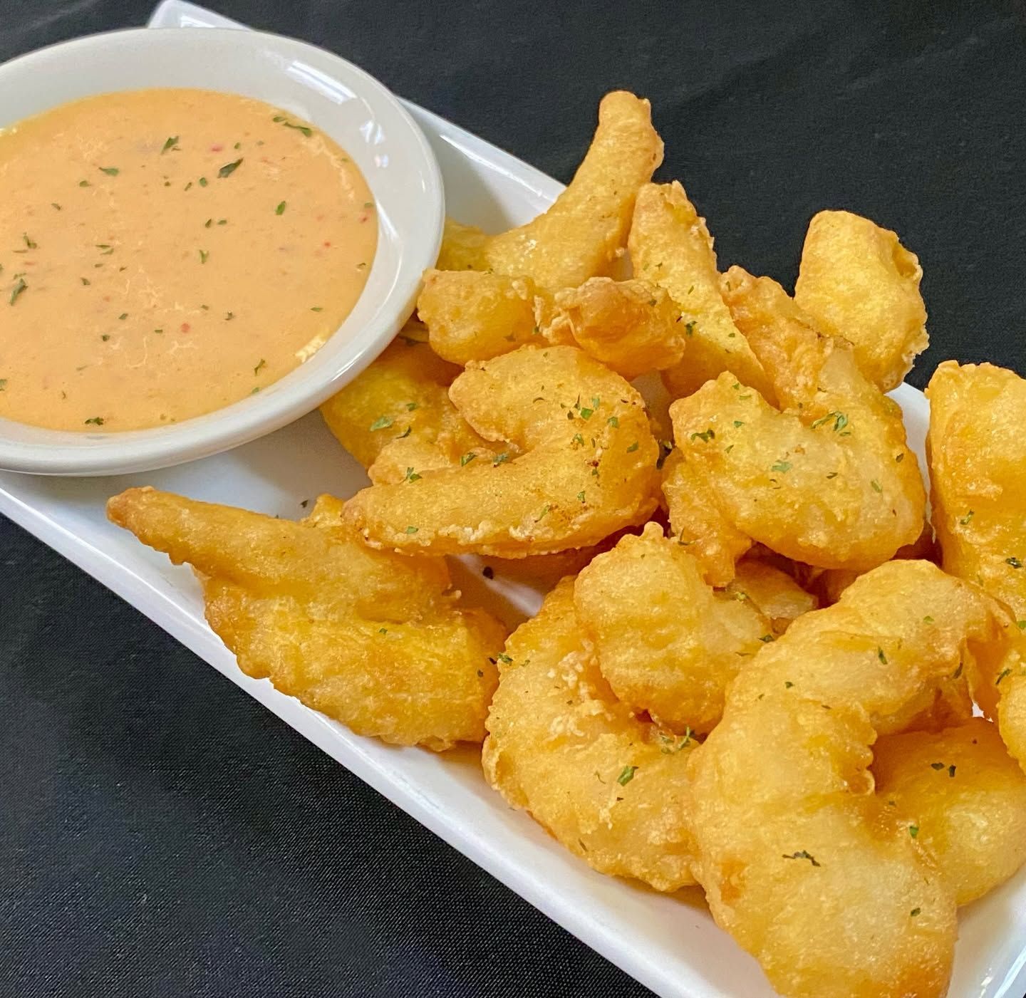 Fried golden shrimp or calamari with a creamy orange dipping sauce on a white plate