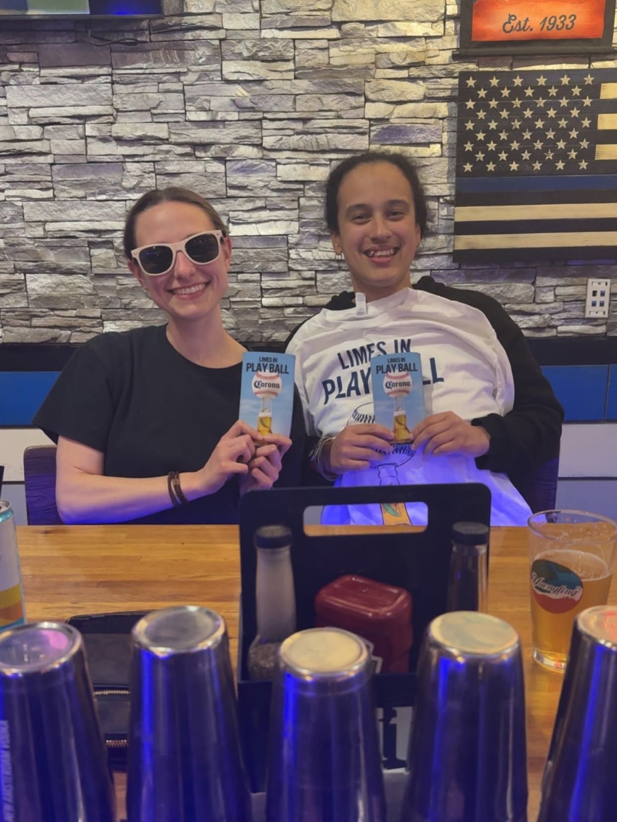 Two people smiling and holding drinks at a bar with an American flag on the wall