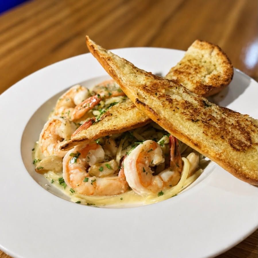 Shrimp pasta in creamy sauce on a white plate, topped with toasted bread slices