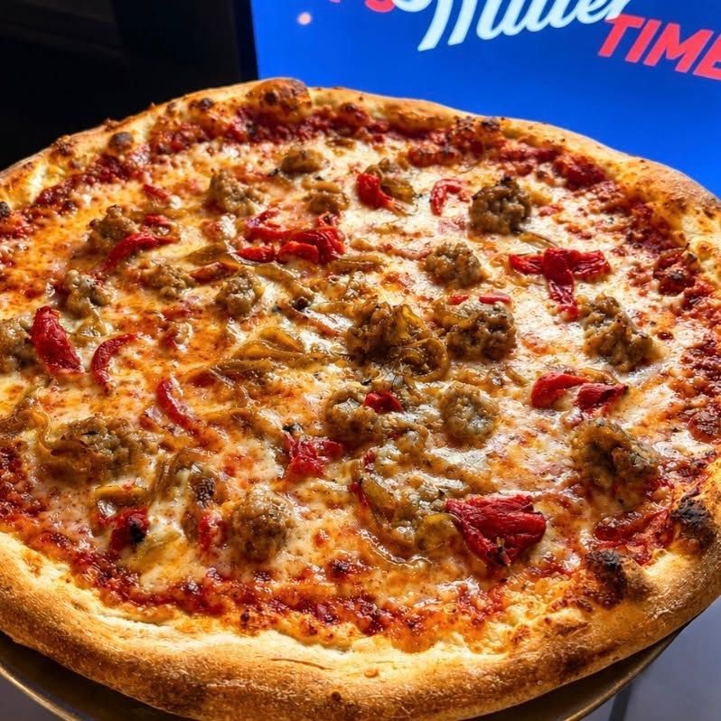 Cheesy pizza topped with sausage and pepperoni on a tray against a blue background