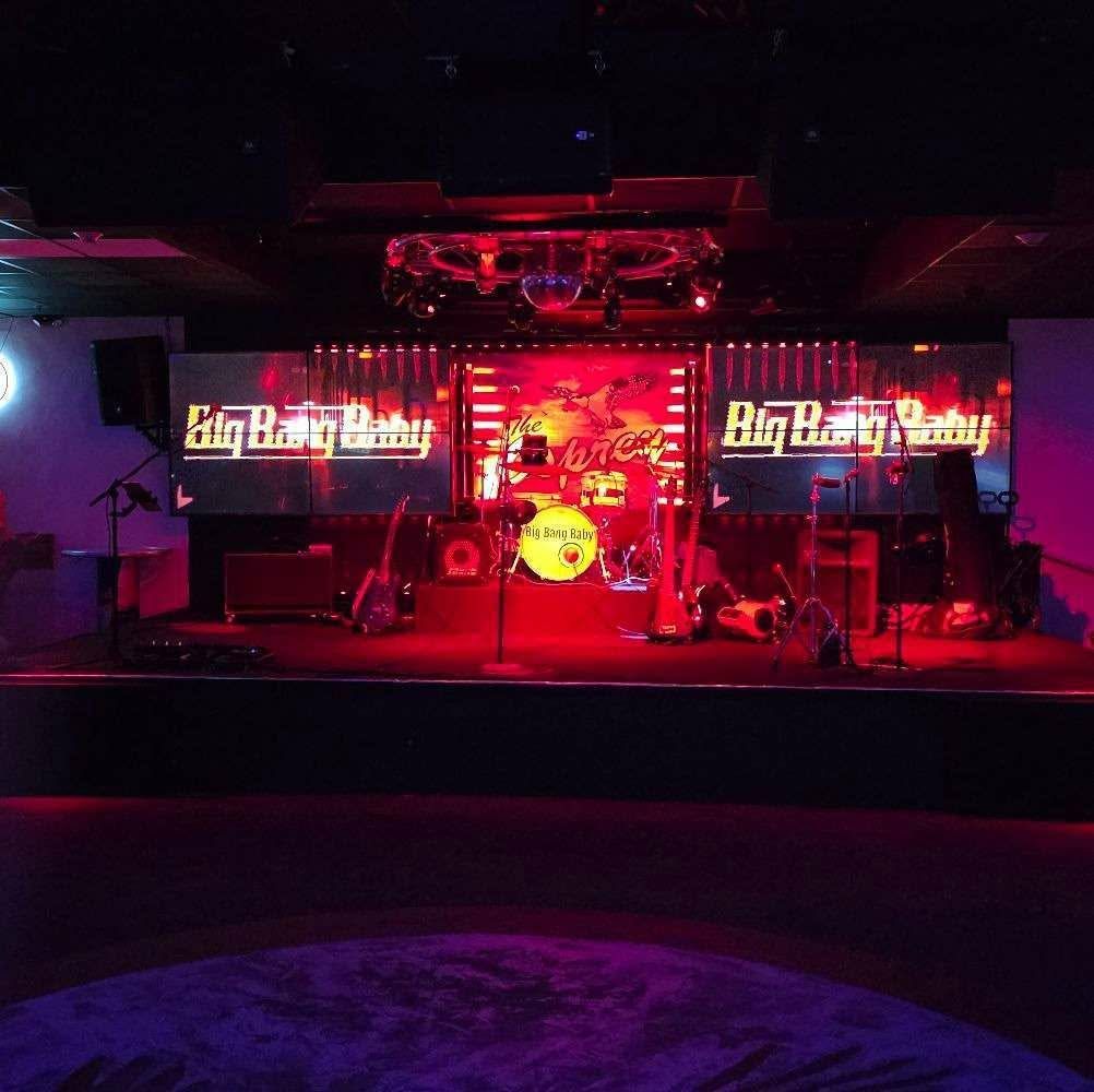 Empty concert stage with red and purple lighting, drums, and Big Hoss signs on both sides