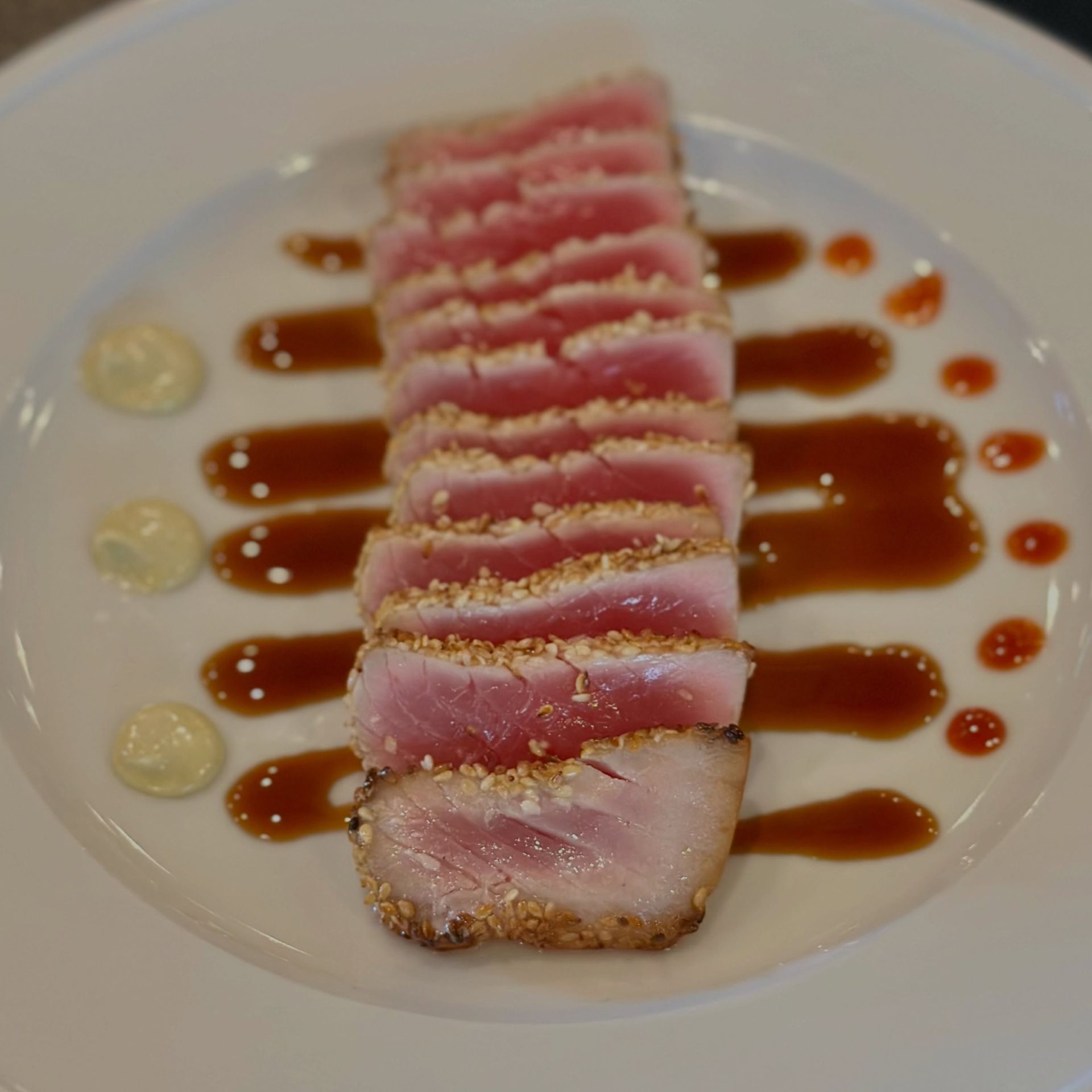 Sliced seared tuna with sauce drizzles and dollops on a white plate
