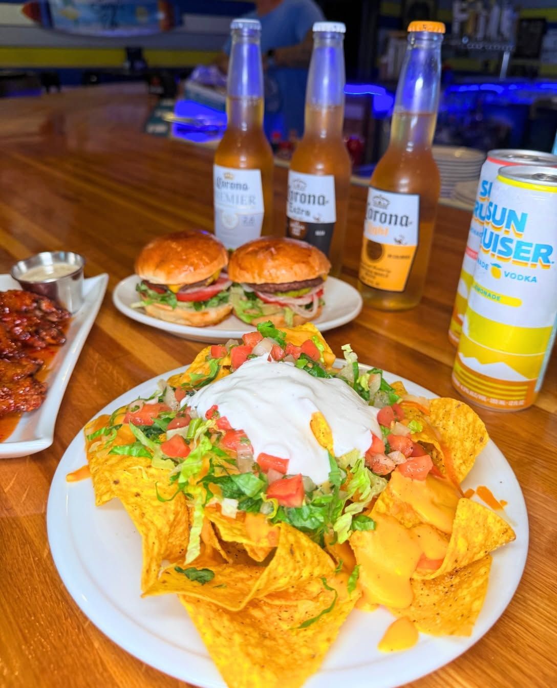 Loaded nachos with salsa and sour cream, burgers, and bottled drinks on a restaurant table.