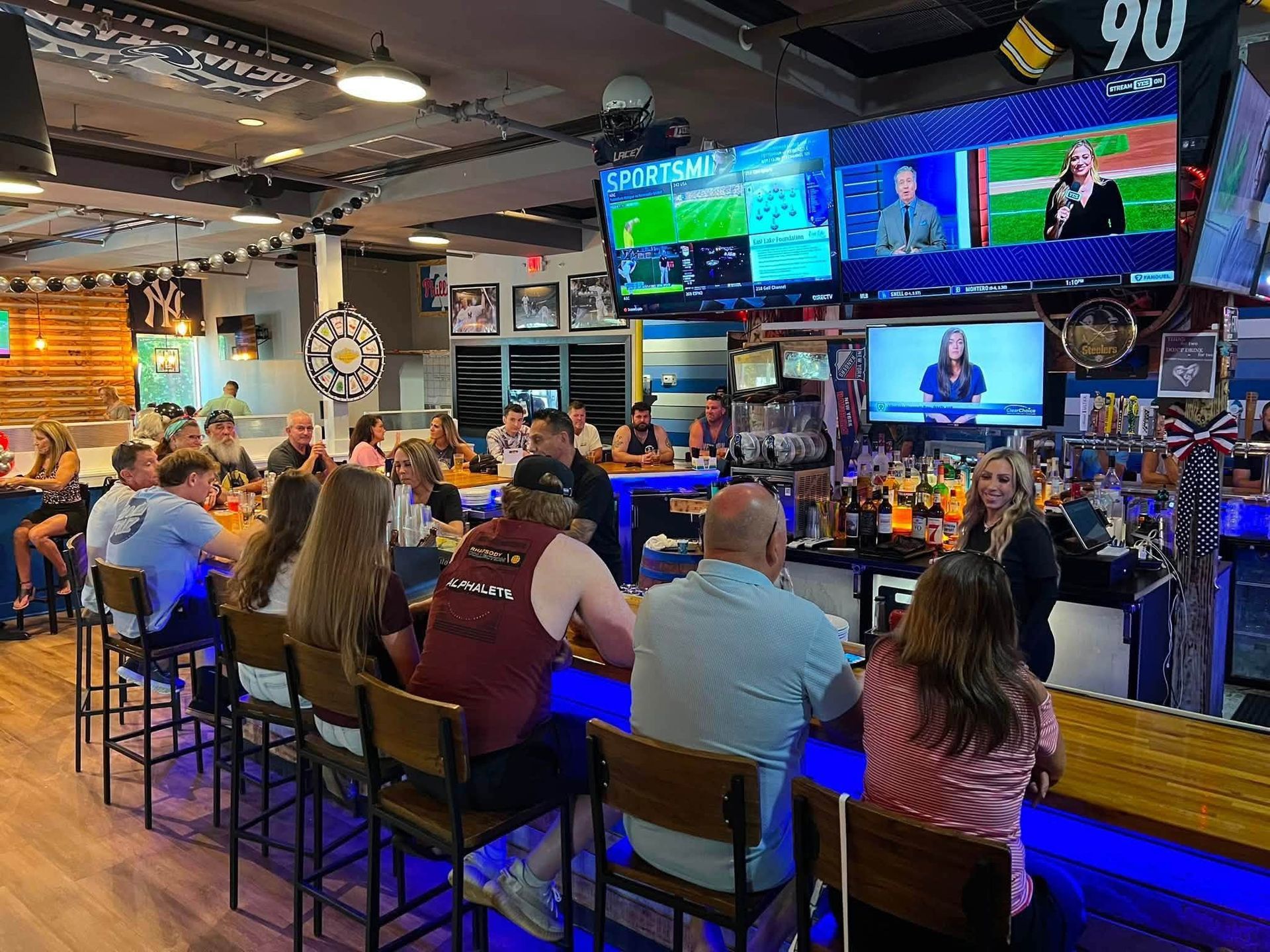 Sports bar with patrons seated at the counter watching multiple TV screens and a live sports broadcast.