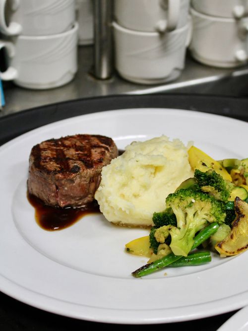 Steak with mashed potatoes and broccoli on a white plate in a kitchen setting