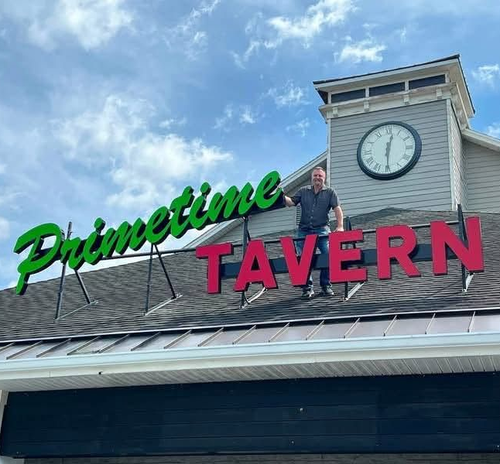 Primetime Tavern sign on a roof with a clock tower and a person standing near the lettering