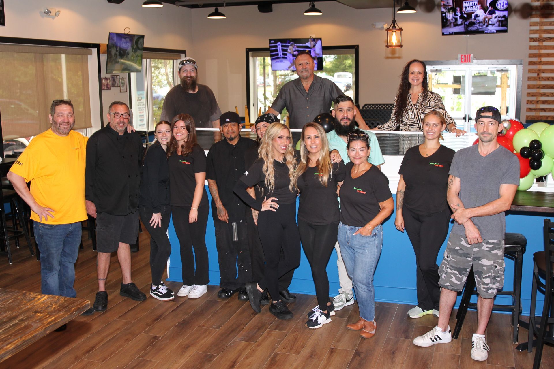 Group of people posing together in a restaurant, smiling and standing on a wooden floor.