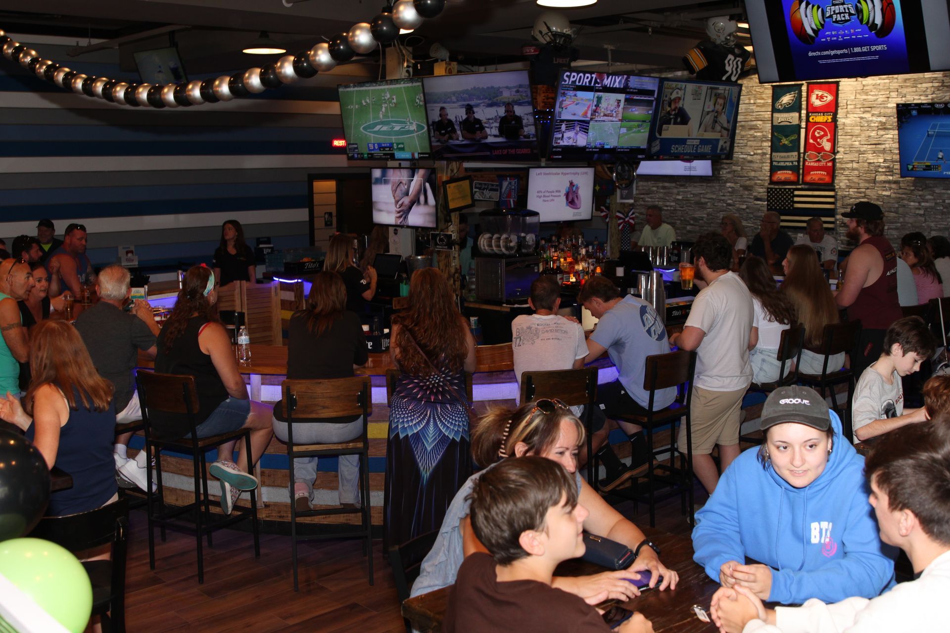Crowded sports bar with patrons seated at tables, watching multiple TV screens above the counter.