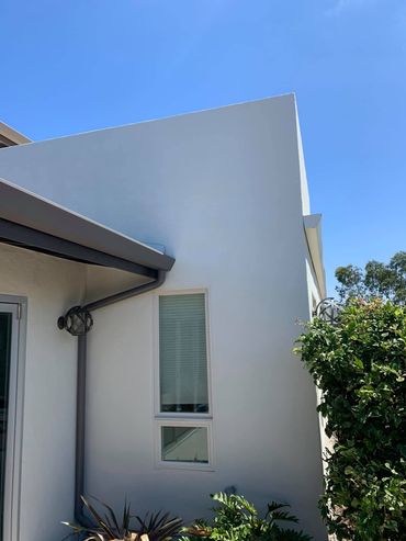 A white house with a window and a gutter on a sunny day.
