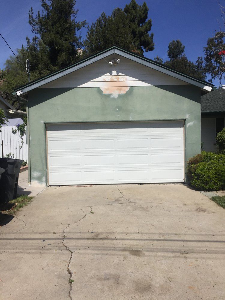 A white garage door is sitting in front of a green house.
