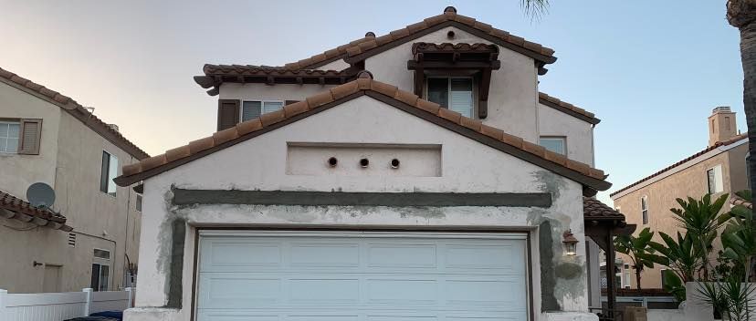 A white house with a brown roof and a white garage door.