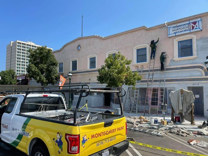 A yellow truck is parked in front of a building being painted.