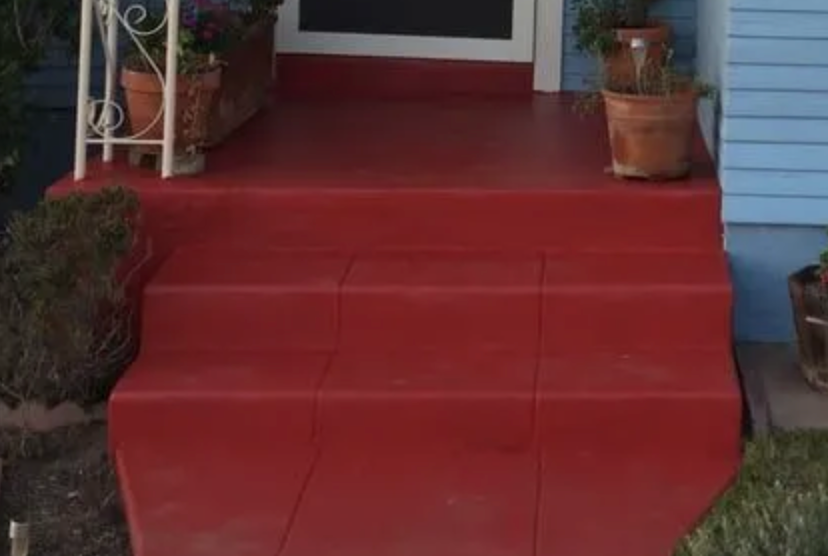 A red porch with potted plants on it and a blue house in the background.