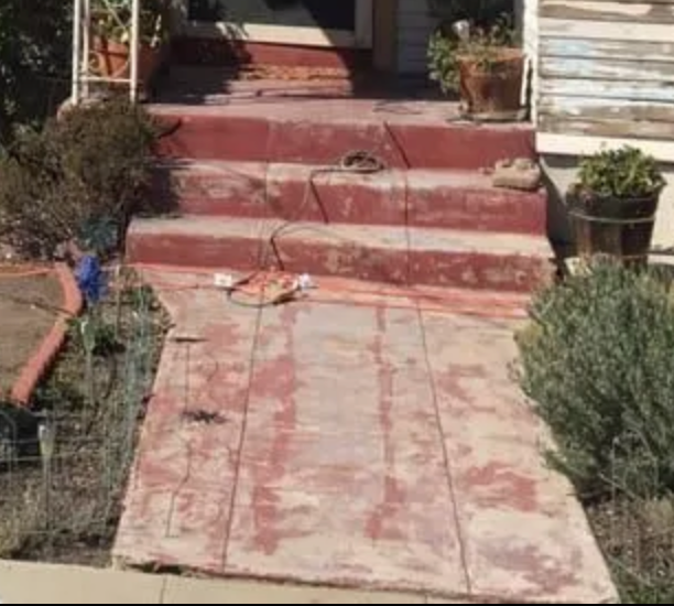 A concrete walkway leading to a house with red steps.