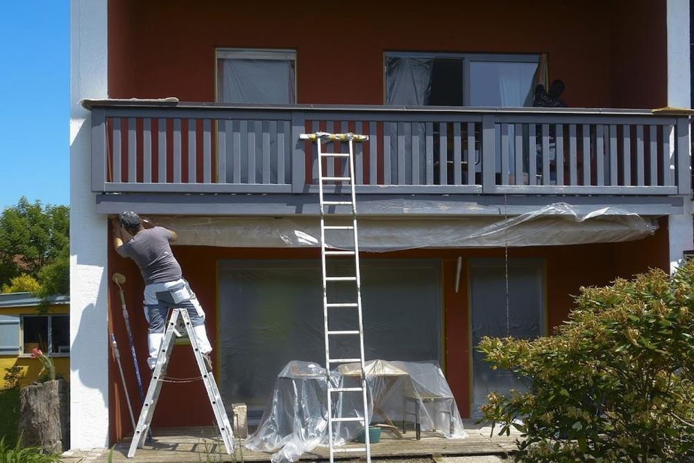 A man on a ladder is painting a balcony of a house