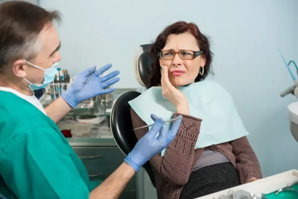 Dentist in blue gloves talking to a smiling patient in a dental chair