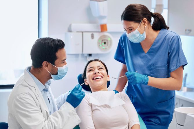 Dentist and dental assistant treating a smiling patient in a clinic, all wearing masks and gloves