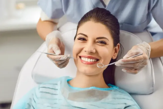 Smiling dental patient in a chair while a dentist holds mirrors near her mouth