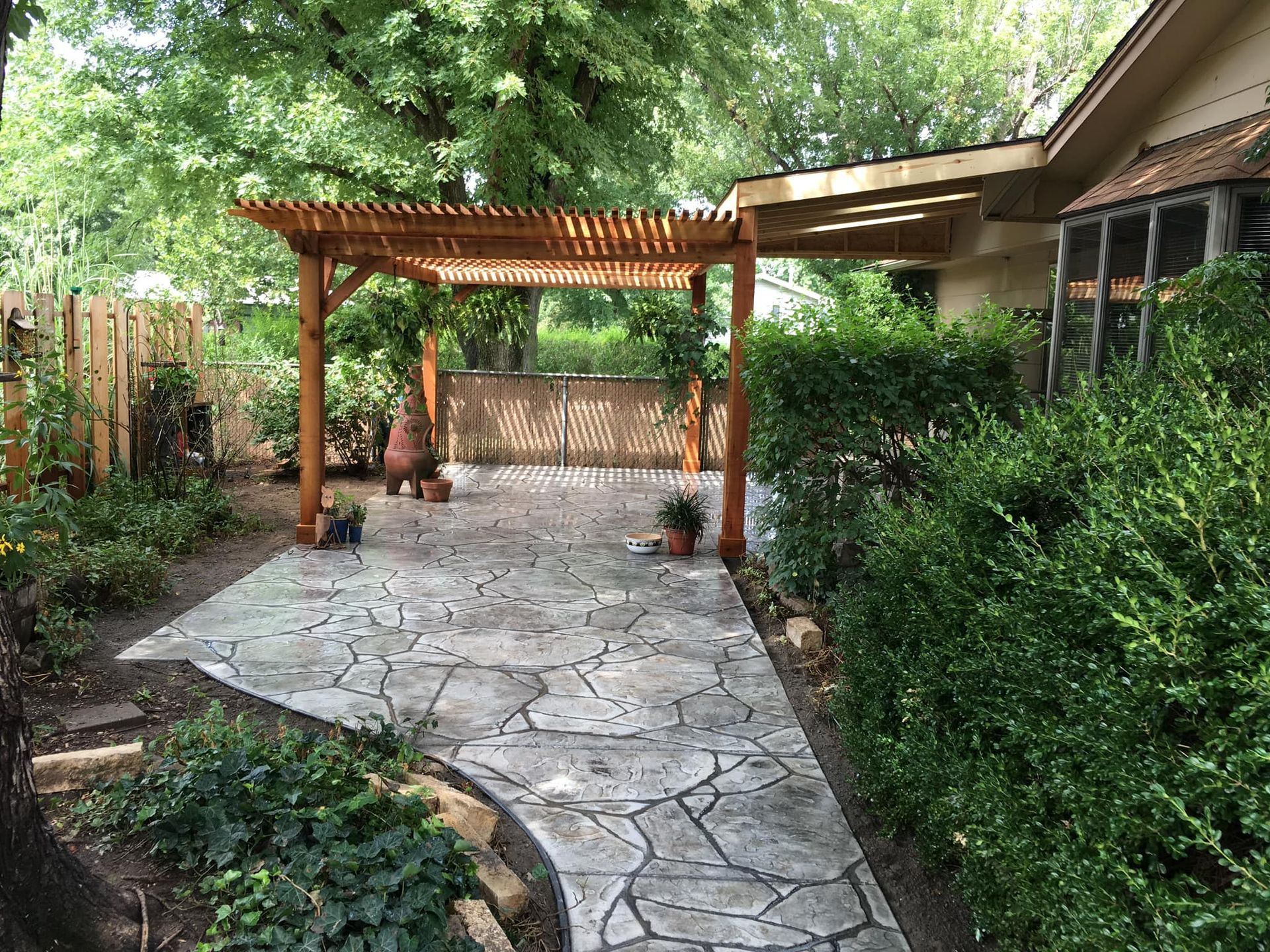 A wooden pergola is sitting on top of a stone patio next to a house.