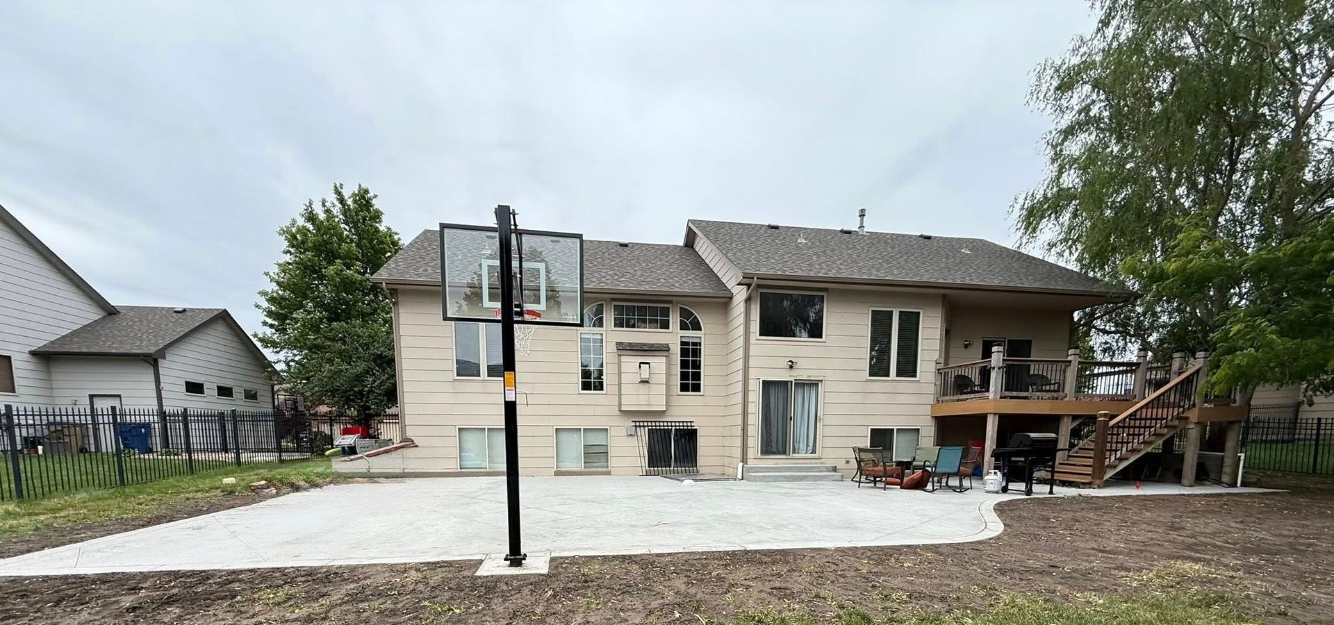 Large poured concrete patio behind a two-story Kansas home with a raised deck