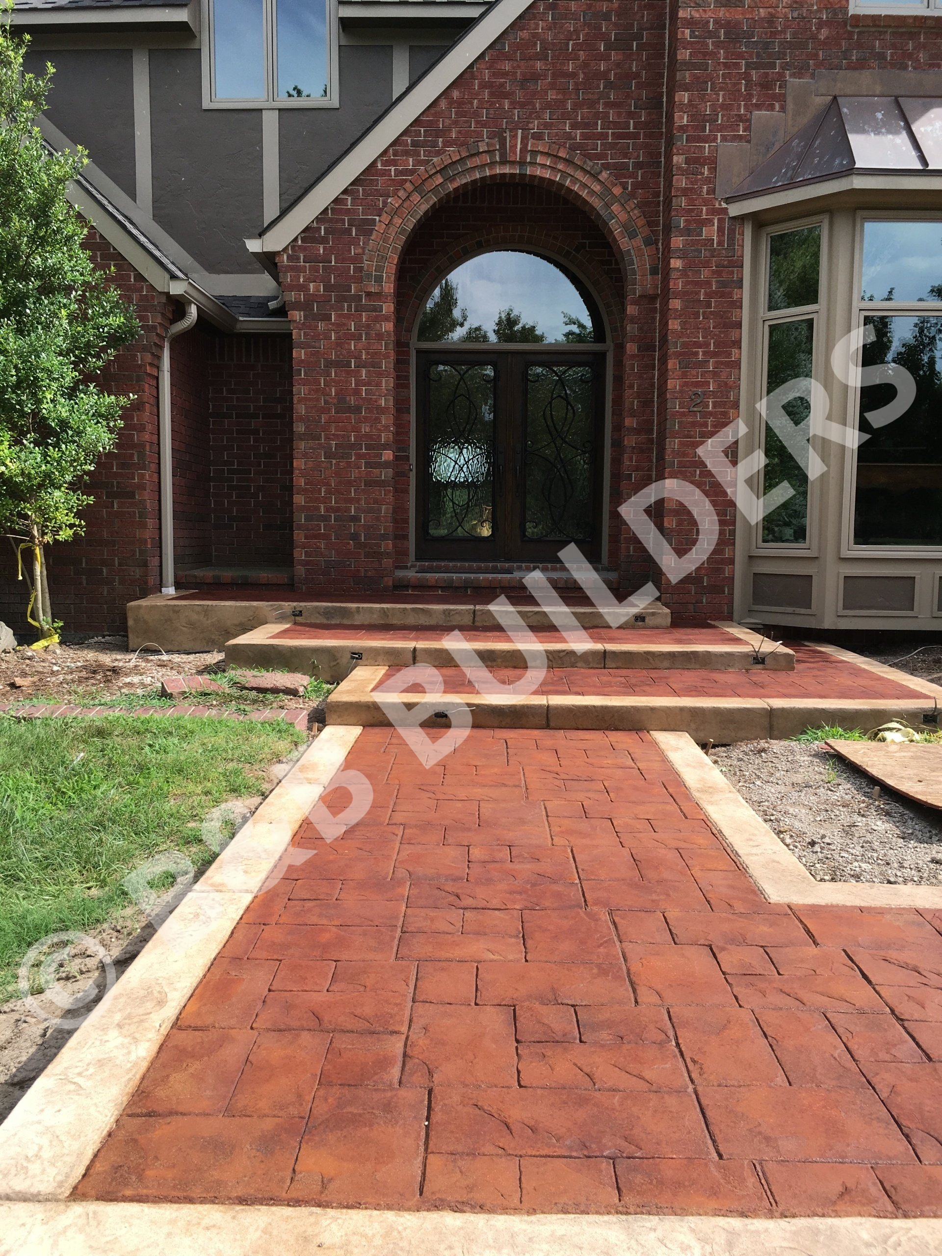 A  tamped concrete entryway path with red faux slate pattern bordered by sandstone