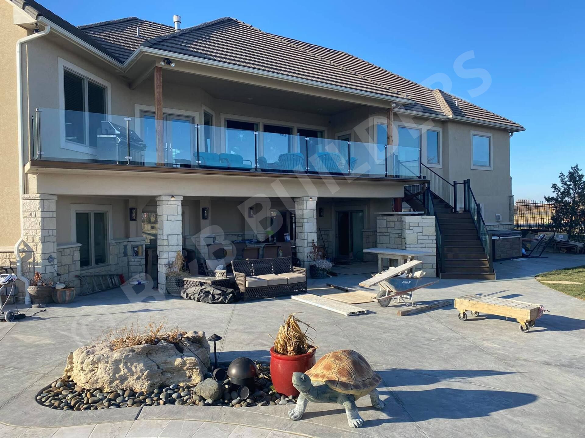 A home with a large deck across almost the entirety of the second floor, with stairs up and more patio space underneath