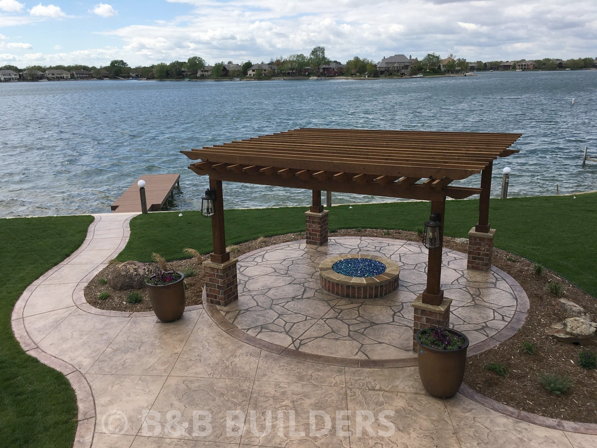 A pergola overlooking a lake with a fire pit in the middle