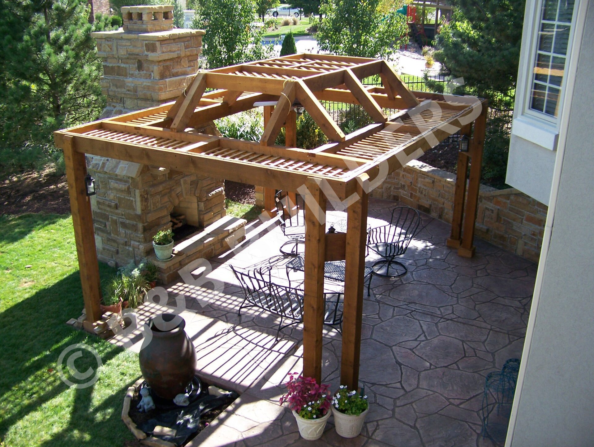 Decorative wooden pergola with masonry fireplace and stamped concrete patio