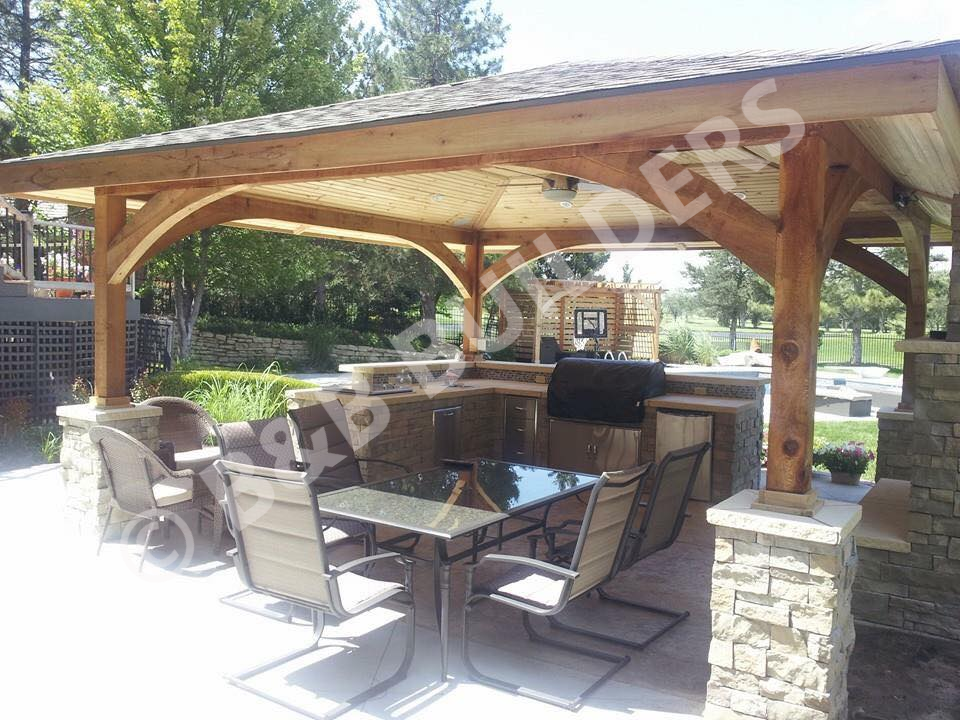 a concrete patio with a stone and wood-framed pergola, offering shade over a dining table and outdoor kitchen area