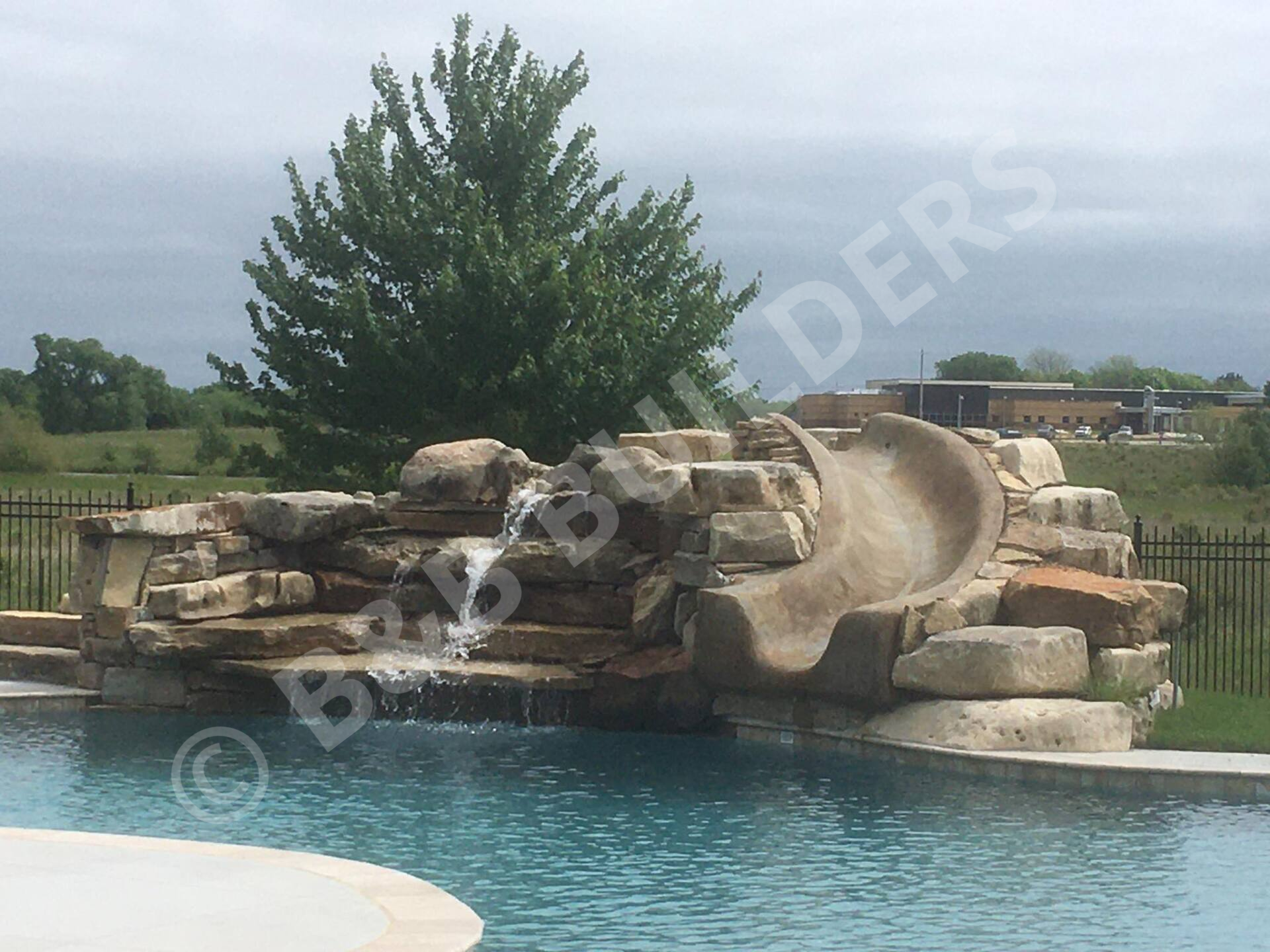 Poolside stacked stone waterfall with waterslide