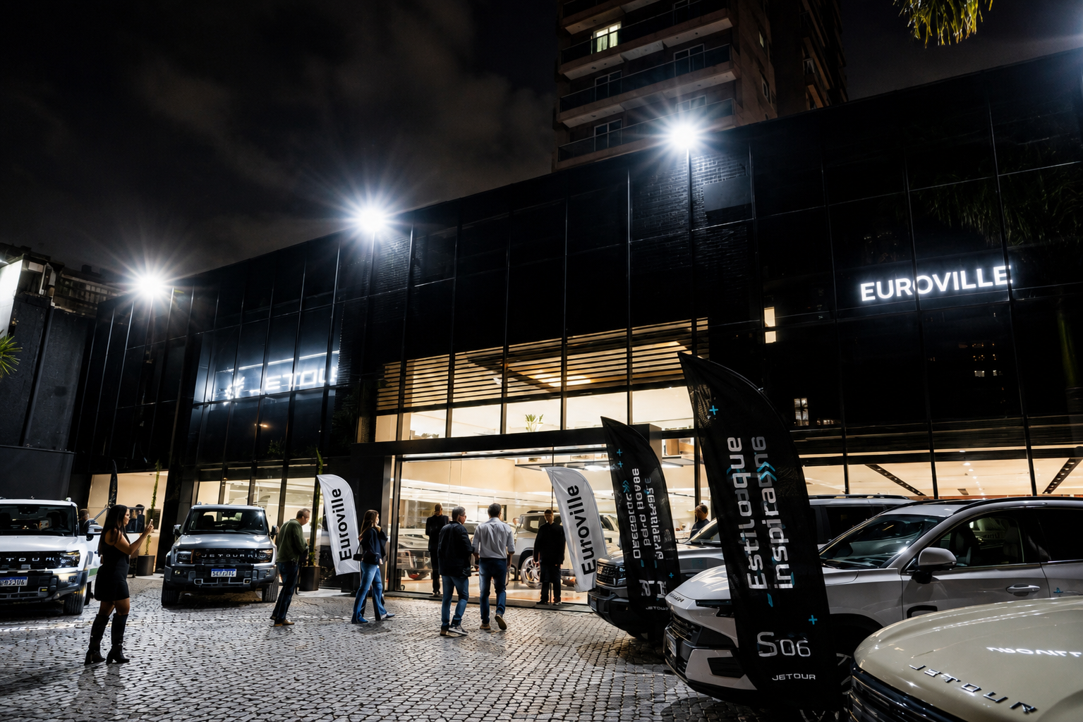 Nighttime outside a glass-fronted Euroville building with parked cars and people under bright lights