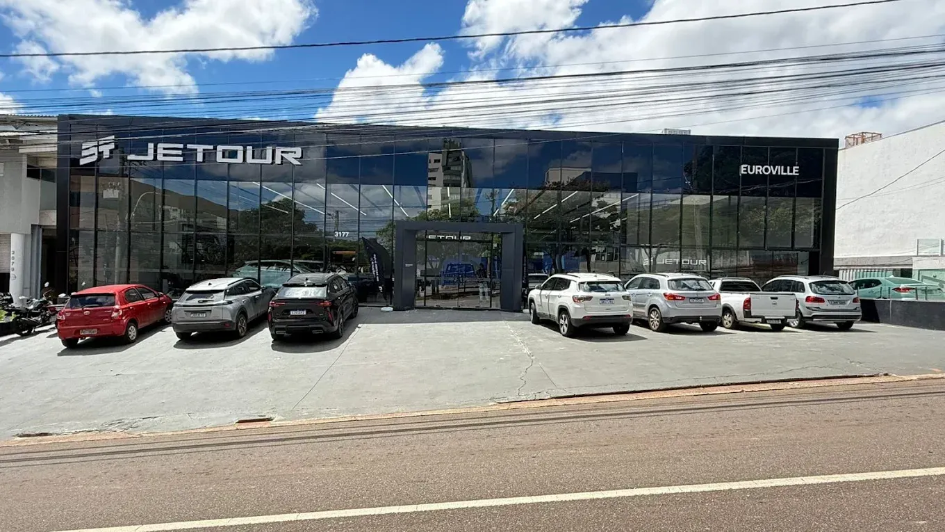 Front view of a Jetour car dealership with several cars parked outside under a blue sky.